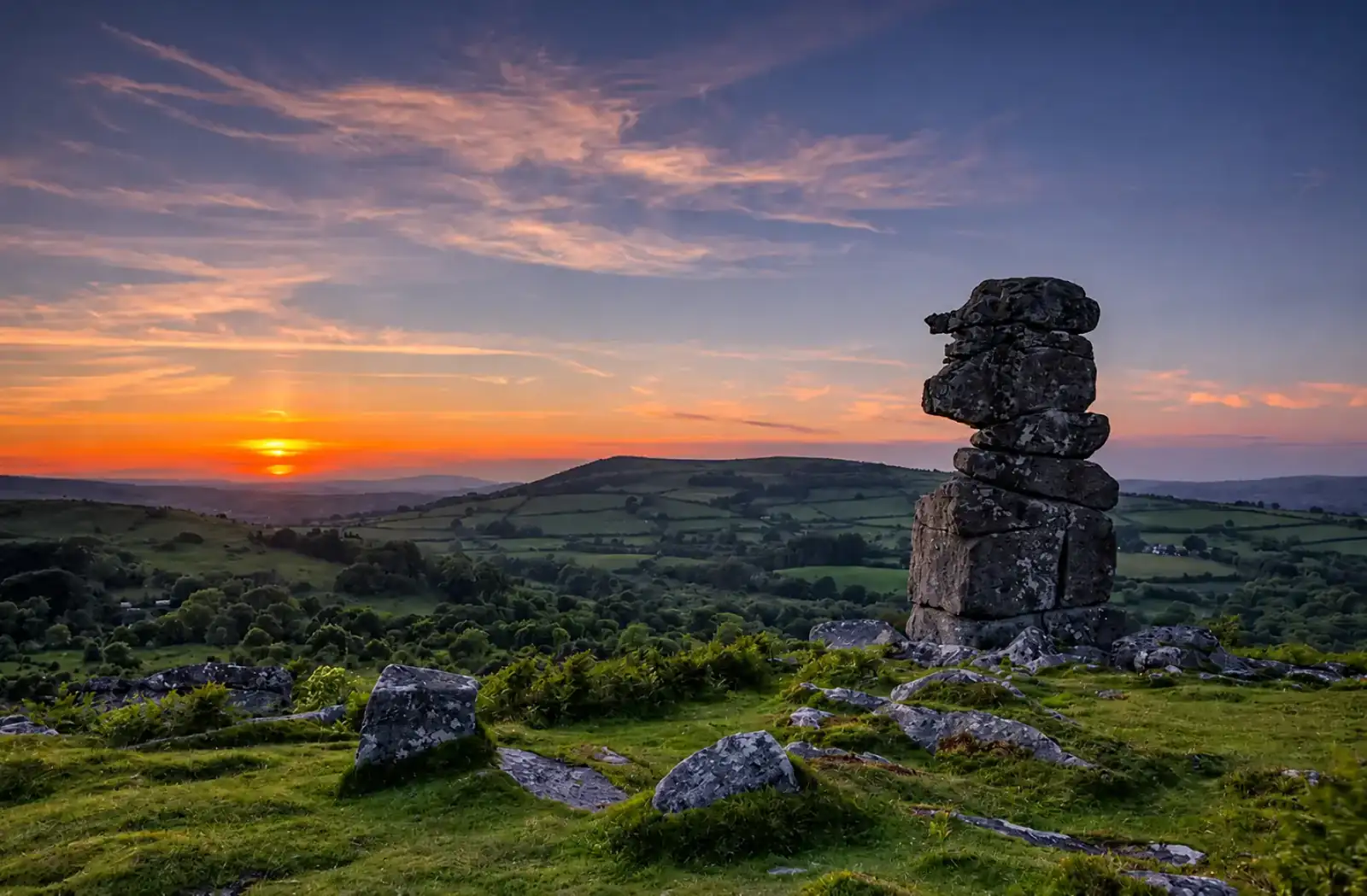 Granite tor on Dartmoor at sunset above green Devon fields